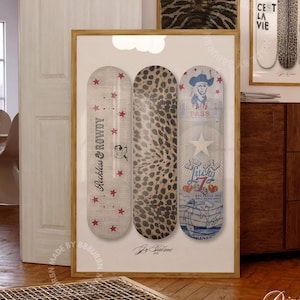 May include: A framed print showcasing three skateboard decks with distinct designs. One deck features a leopard print, another has the text "Reckless & Rowdy" and stars, and the third has a cowboy graphic. The print is displayed in a room with other art.