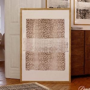 May include: Three framed abstract art prints with neutral tones. The largest print features a brown dotted pattern with a white horizontal band. Two smaller prints display animal print patterns. The frames are a light brown color.