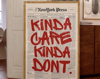 May include: A framed vertical wall art print featuring a vintage newspaper layout titled The NewYork Press. The center displays the bold red hand-lettered text KINDA CARE KINDA DONT. The background consists of columns of small black printed text.