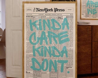 May include: A framed wall art print featuring a vintage newspaper layout titled The NewYork Press with the text KINDA CARE KINDA DONT written in large, bold, light blue brushstroke lettering across the center of the page in a vertical orientation.