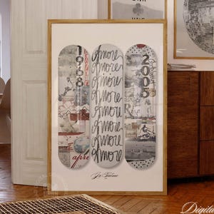May include: A framed art print showing three skateboard decks with the word "Amore" in cursive. The decks have collage designs with numbers and images. The print is in a room with other framed art and a wooden cabinet.