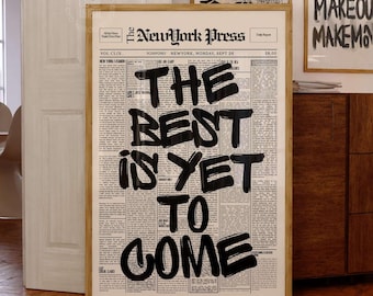 May include: A framed vertical wall art print featuring a vintage newspaper layout titled The NewYork Press. The design displays bold, black, hand-lettered brushstroke text that reads THE BEST IS YET TO COME centered over columns of small black text.