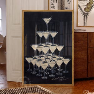 May include: A framed print depicting a pyramid of martini glasses, each filled with a pale liquid. The artwork has a dark background and the text "Extra Party Please reserve". Other framed art pieces are visible in the background, with a wooden frame.