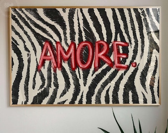 May include: A rectangular wall art print in a gold frame featuring a black and white zebra stripe pattern background with the word AMORE. written in bold red, hand-drawn style lettering across the center of the print.