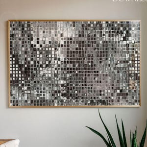May include: A rectangular wall art piece featuring a grid of small, reflective silver and gray square tiles that create a shimmering, mirrored mosaic effect, enclosed within a thin, metallic gold frame that highlights the textured surface.