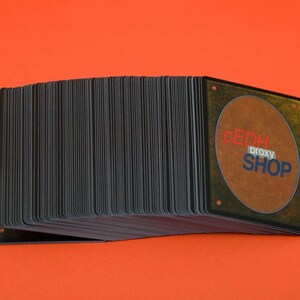 May include: A deck of playing cards with black edges and the text "CEDH proxy SHOP" on the back. The cards are stacked on an orange background.