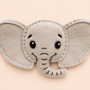 May include: A light gray felt elephant applique featuring large ears, a curved trunk, and embroidered black details for the eyes, eyebrows, and mouth. The edges of the elephant shape are finished with a visible light gray blanket stitch.