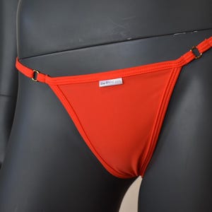 May include: Red thong underwear with thin straps and a small logo tag that reads "big-knickers.com".