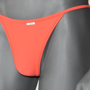 Peut inclure: Un sous-vêtement de couleur orange vif, taille basse, de style string avec une fine ceinture.