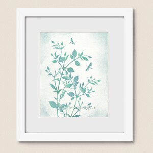 May include: A watercolor painting of a leafy branch with delicate green leaves and two dragonflies in flight against a light blue background. The painting is framed in a white frame.