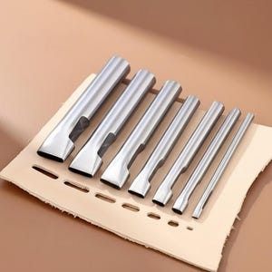 May include: A collection of seven silver metal leather working tools of different sizes, displayed on a piece of tan leather with punched holes. The tools have a rectangular cutting edge and a cylindrical handle.