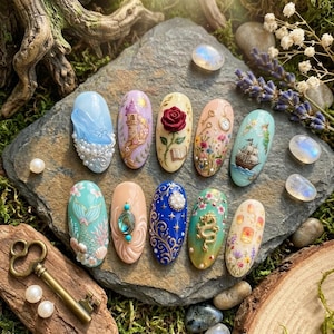 May include: A collection of ten intricately designed nail art pieces. Each nail features a unique design, including a castle, a rose, a ship, and a mermaid. The nails are set on a gray stone surface, surrounded by natural elements like moss and crystals.