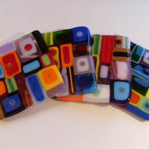 May include: Set of five colorful glass coasters with geometric patterns. Each coaster features a different combination of red, yellow, blue, green, and white squares and rectangles.