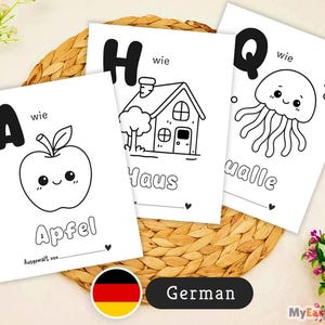 May include: Three white flashcards with black outlines of an apple, house, and jellyfish, each with a letter and word in German. The cards are on a woven, circular placemat. The word "Apfel" is under the apple illustration.