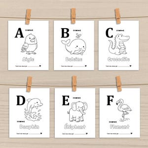 Peut inclure: Six cartes blanches avec des contours noirs d'animaux, chacune avec une lettre de l'alphabet. Les cartes sont accroch&eacute;es &agrave; une ficelle avec des pinces &agrave; linge en bois. Les animaux incluent un aigle, une baleine, un crocodile, un dauphin, un &eacute;l&eacute;phant et un flamant.