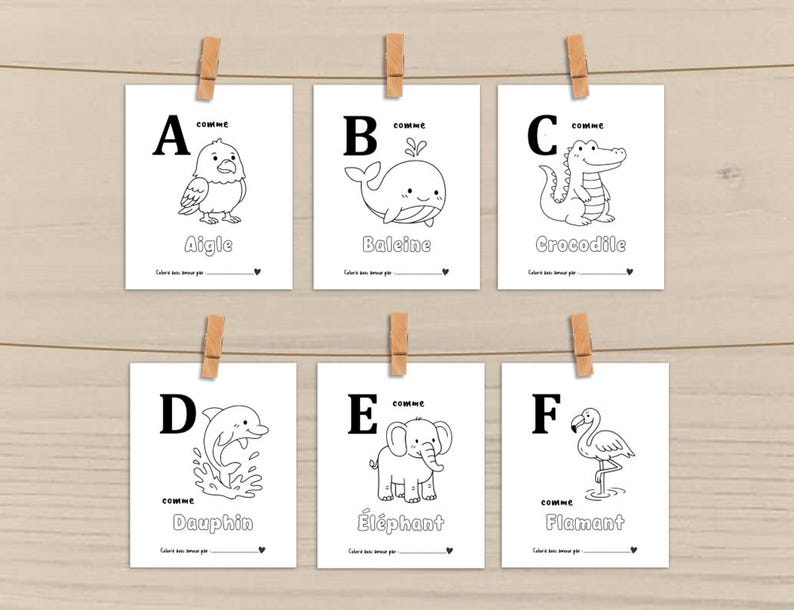 Peut inclure: Six cartes blanches avec des contours noirs d'animaux, chacune avec une lettre de l'alphabet. Les cartes sont accroch&eacute;es &agrave; une ficelle avec des pinces &agrave; linge en bois. Les animaux incluent un aigle, une baleine, un crocodile, un dauphin, un &eacute;l&eacute;phant et un flamant.
