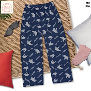 May include: Navy blue pajama pants with a repeating pattern of gray eagles and the word "Seattle." The pants are part of a sleepwear set, with a matching sleep mask and socks.