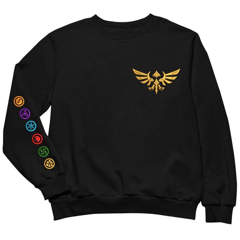 May include: Black sweatshirt with a gold embroidered emblem on the chest and colorful circular symbols on the left sleeve. The emblem features a stylized bird with outstretched wings. The symbols are in various colors.