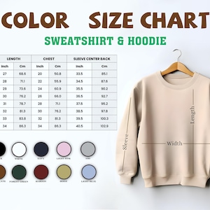 May include: A beige sweatshirt hanging on a wooden hanger, with a size chart and color options displayed. The chart shows measurements in inches and centimeters for length, chest, and sleeve center back. Color options include black, white, navy, and light pink.