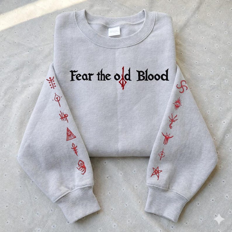 May include: A light gray sweatshirt with the text "Fear the old Blood" in black and red. The sleeves feature red symbols. The sweatshirt has a crew neck and long sleeves.