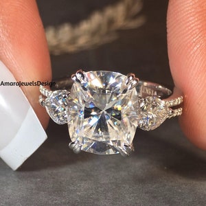 May include: A silver ring featuring a large, square-shaped, clear gemstone flanked by two smaller pear-shaped, clear gemstones.