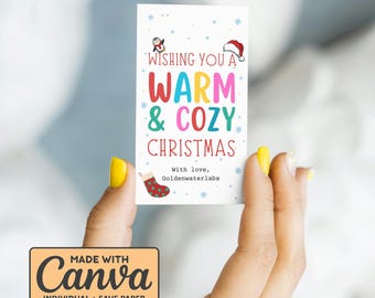 Può includere: Un biglietto di Natale rettangolare con la scritta "Wishing You a Warm & Cozy Christmas" in lettere colorate. Il biglietto presenta illustrazioni di un pinguino, un cappello di Babbo Natale, fiocchi di neve e una calza natalizia. Il biglietto è tenuto da una persona.