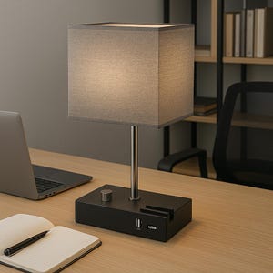 May include: A modern desk lamp with a gray square lampshade and a black base. The lamp has a silver stem and a USB port. The lamp is on a wooden desk with a laptop and a notebook.