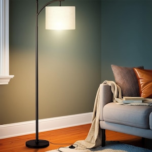 May include: A black arc floor lamp with a rectangular lampshade. The lamp is positioned next to a window and a gray sofa with decorative pillows. The room has hardwood floors and a neutral color palette.