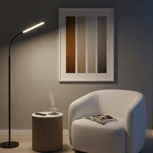 May include: A modern living room scene featuring a black floor lamp with an illuminated head, a white armchair, and a small side table. A framed artwork with vertical color blocks hangs on the wall. A cup of coffee steams on the table, and a magazine rests on the chair.