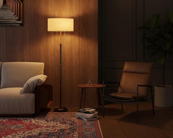 May include: A living room scene featuring a cream-colored sofa, a brown leather armchair, and a floor lamp with a rectangular lampshade. A small round table holds a glass. A patterned rug and a potted plant complete the decor.