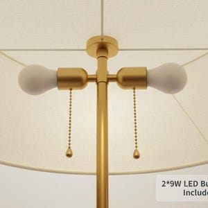 Pu&ograve; includere: Una lampada color oro con un paralume color crema. La lampada ha due lampadine e catenelle. Il testo "2*9W LED Bulb Included" &egrave; visibile nell'angolo in basso a destra. La lampada &egrave; progettata per uso interno.