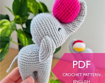 May include: A crocheted gray elephant toy with a bright pink ball balanced on its trunk. The elephant has small black eyes and large ears. The image also includes text that says "PDF CROCHET PATTERN ENGLISH".