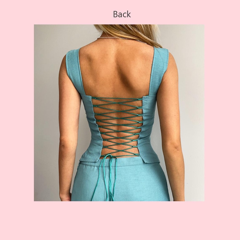 May include: A light blue top and skirt set with a square neckline and a laced-up back. The back of the top features a crisscross design with green cording. The outfit is made of a textured fabric and is shown from the back.