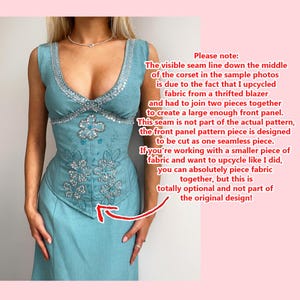 May include: A light blue corset-style dress with intricate floral embroidery and silver beading. The dress features a V-neckline and a fitted bodice, with a flared skirt. The text in the image explains the seam line is due to upcycled fabric.