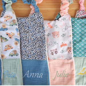 May include: A selection of personalised baby bibs in different patterns and colours. One bib has cars with animal drivers, another a blue floral design, and a third displays woodland creatures. Each bib is embroidered with a name in a matching colour.