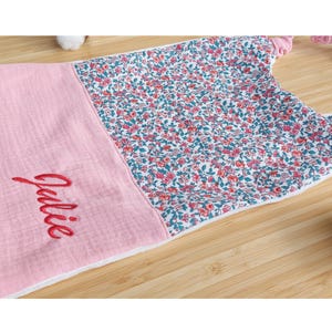 May include: A baby bib with a pink section and a floral pattern. The name "Julie" is embroidered in red script on the pink section. The floral pattern features red and pink flowers with green leaves on a white background. The bib has a white border.