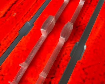 May include: Two clear plastic pieces with a curved shape at one end and a straight edge at the other. The pieces are on a red surface.