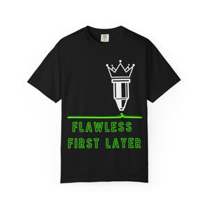 Może przedstawiać: Czarny t-shirt z krótkim rękawem z białą grafiką dyszy drukarki 3D zwieńczonej koroną. Pod dyszą znajduje się pozioma neonowo-zielona linia oraz napis FLAWLESS FIRST LAYER wykonany neonowo-zielonymi wielkimi literami.