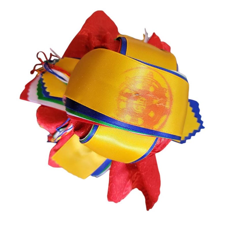 May include: A decorative, layered ornament featuring bright red fabric and yellow satin ribbons. The yellow ribbons have a blue trim and a printed design. The ornament also includes colorful ribbons and is set against a white background.