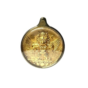 Könnte beinhalten: Goldfarbener Anhänger mit detailliertem Relief einer mythischen Kreatur. Der runde Anhänger hat eine Schlaufe für eine Kette. Die Kreatur hat Flügel und ein verziertes Gesicht. Der Anhänger ist wahrscheinlich aus Metall.
