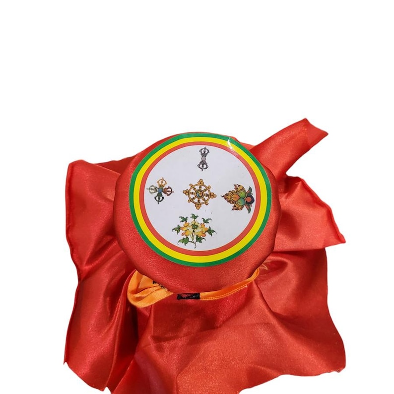 K&ouml;nnte beinhalten: Ein roter Zeremonienhut mit einem kreisf&ouml;rmigen Emblem mit verschiedenen Symbolen und einem gelb, gr&uuml;n und rot umrandeten Rand. Der Hut besteht aus einem gl&auml;nzenden, seidigen Material.