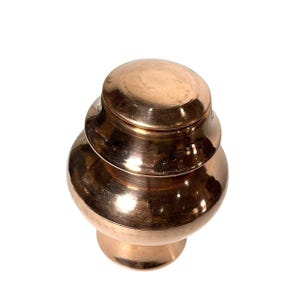 May include: A copper-coloured, tiered container with a lid. The container has a rounded base and a series of stacked, bulbous sections leading up to a domed lid. The surface reflects light, highlighting its polished finish. The item is likely a decorative storage vessel.