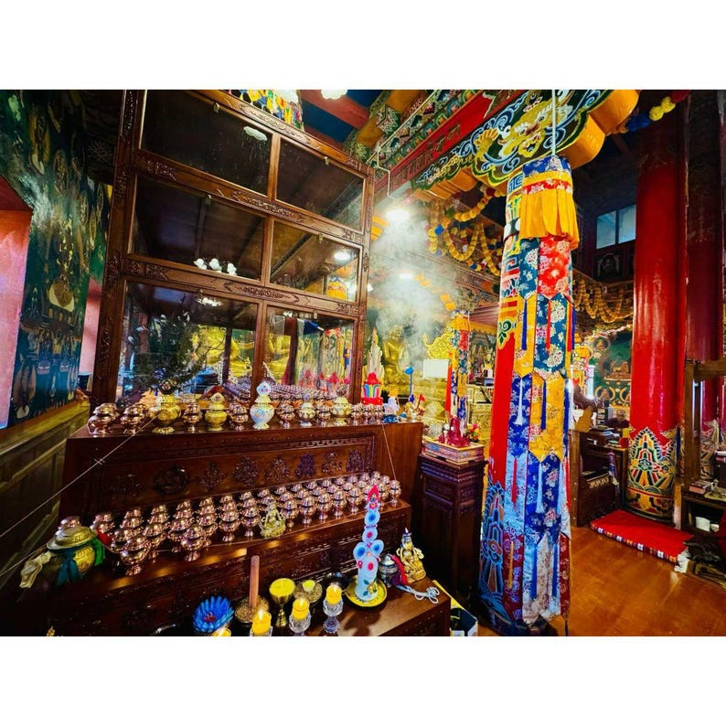 May include: An interior view of a temple, showcasing elaborate wooden furnishings and vibrant decorations. A large wooden cabinet with glass shelves displays various items. Incense smoke is visible, and a tall, decorated pillar stands out. The scene is rich in detail and cultural significance.