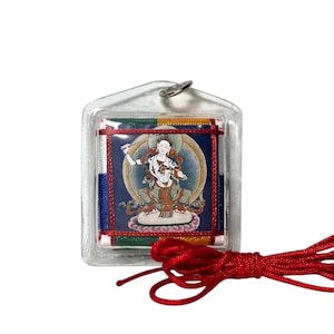 Puede incluir: Colgante cuadrado de plástico transparente con una imagen religiosa. La imagen presenta una figura en un círculo azul y dorado, rodeada de adornos coloridos. Una cuerda roja está unida al colgante.