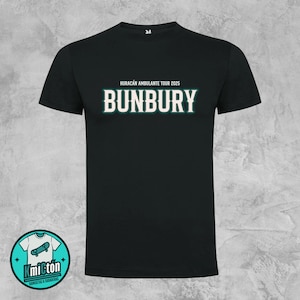 Puede incluir: Camiseta negra con el texto "HURACÁN AMBULANTE TOUR 2025" sobre la palabra "BUNBURY" en negrita, fuente blanca con contorno verde azulado. Un logotipo circular con un monopatín está en la esquina inferior izquierda.
