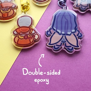 May include: A collection of acrylic keychains featuring various cartoon characters with glossy epoxy finishes. The keychains include yellow and purple lobster clasps. Text on the image reads: Double-sided epoxy with an arrow pointing upward.