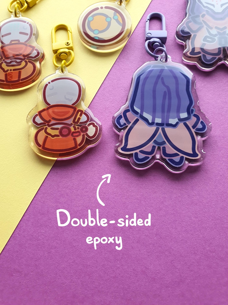 May include: A collection of acrylic keychains featuring various cartoon characters with glossy epoxy finishes. The keychains include yellow and purple lobster clasps. Text on the image reads: Double-sided epoxy with an arrow pointing upward.
