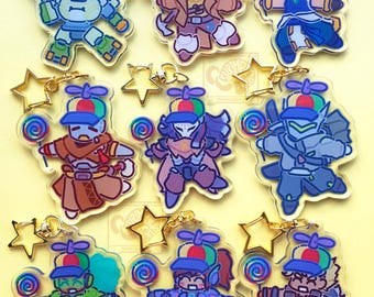 May include: A collection of nine clear acrylic keychains featuring various cartoon characters wearing colorful propeller hats and holding spiral lollipops. Each keychain is attached to a gold-toned star-shaped metal clasp.