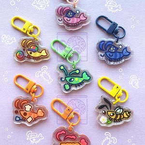 Puede incluir: Una colección de siete llaveros de acrílico transparente con personajes de dibujos animados de camarones y abejas en varios colores, incluyendo rosa, amarillo, azul, verde, naranja y marrón, cada uno con un cierre de mosquetón a juego.