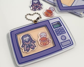 May include: A clear acrylic keychain featuring a purple microwave design with a digital display showing "80:07". The keychain includes two cartoon character charms and a small chain. Additional charms are scattered around.